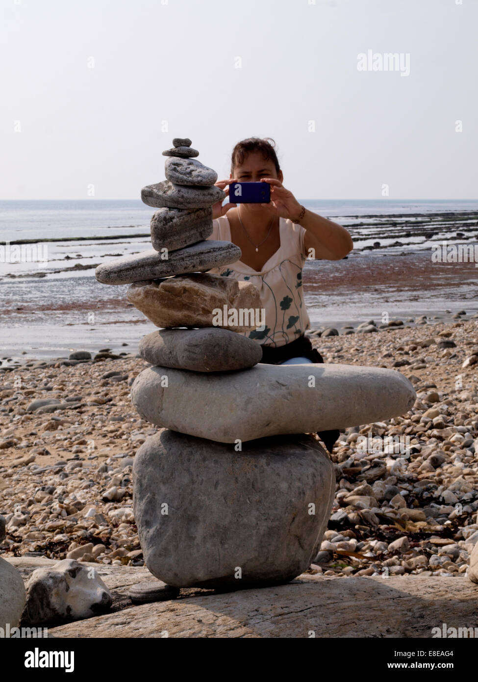 Frau fotografieren einen Stapel von Kiesel am Strand mit Handy, Lyme Regis, Dorset, Großbritannien Stockfoto