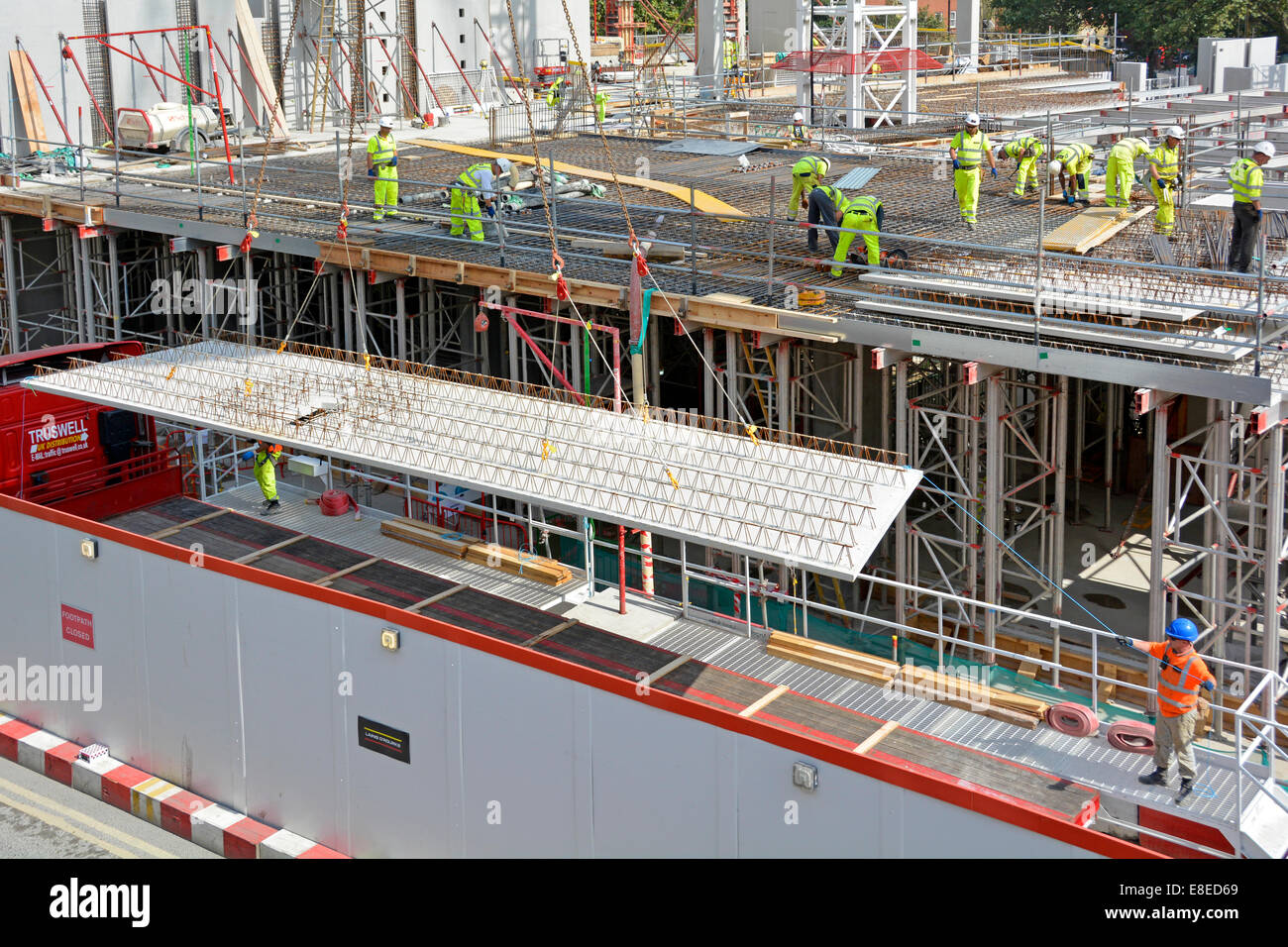Baustellenarbeiten werden durchgeführt beschäftigte Arbeiter, Hochsichtskit und Schutzhelm über man und Kran heben Betonbodenplatte LKW Großbritannien Stockfoto