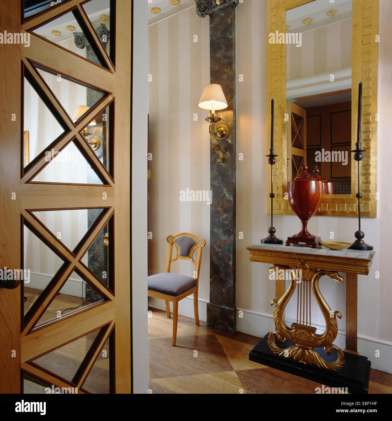 Spiegel über verzierten Konsolentisch mit hohen Kerzen in eleganten Halle mit gestreiften Tapeten und eckig gerahmt verglaste Tür Stockfoto