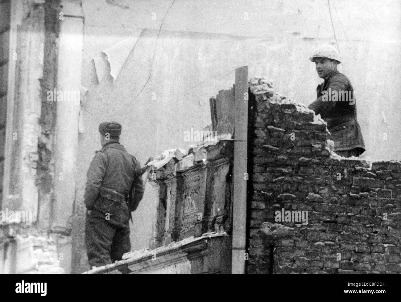 Abbrucharbeiten von Grenze Häusern wird unter der Obhut bewaffneten Grenzsoldaten in der Bernauer Straße in Berlin am 16. Februar 1966 fortgesetzt. Stockfoto