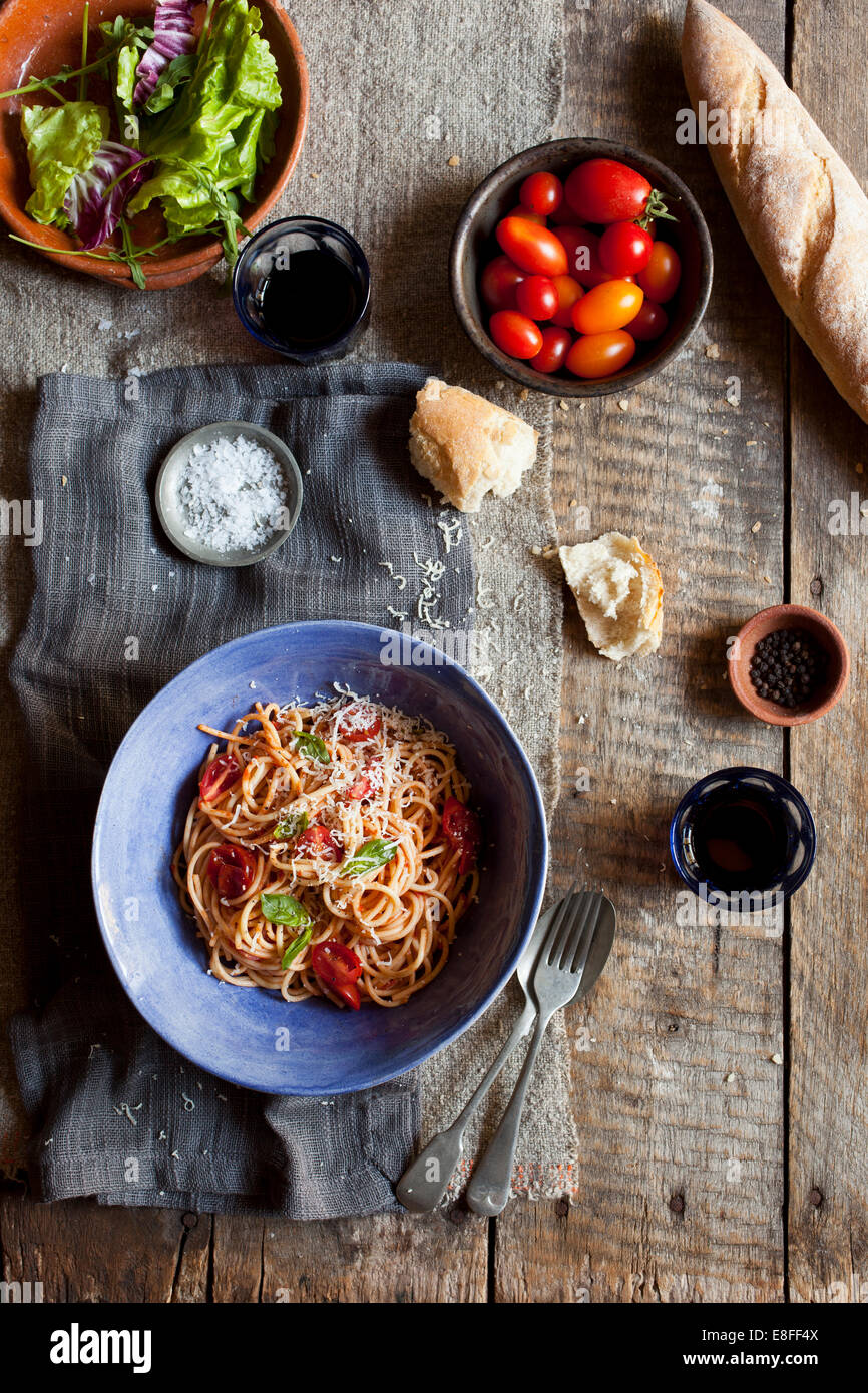 Blick von oben auf eine Schüssel Tomaten, Basilikum und Parmesan Spaghetti mit einer Schüssel Salat und Baguette Stockfoto