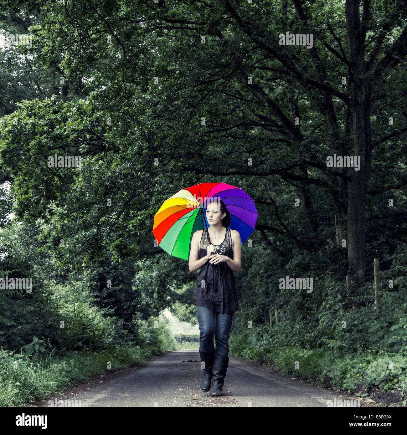 Frau, die die Straße hinunter geht, mit einem bunten Regenschirm Stockfoto