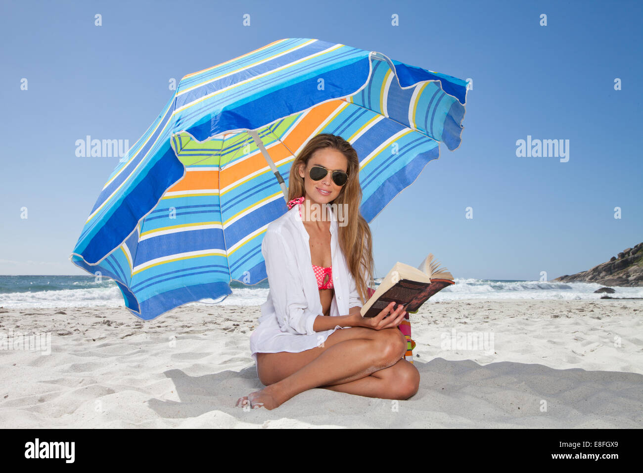 Frau, die ein Buch am Strand liest, unter einem Sonnenschirm sitzt, Kapstadt, Westkap, Südafrika Stockfoto