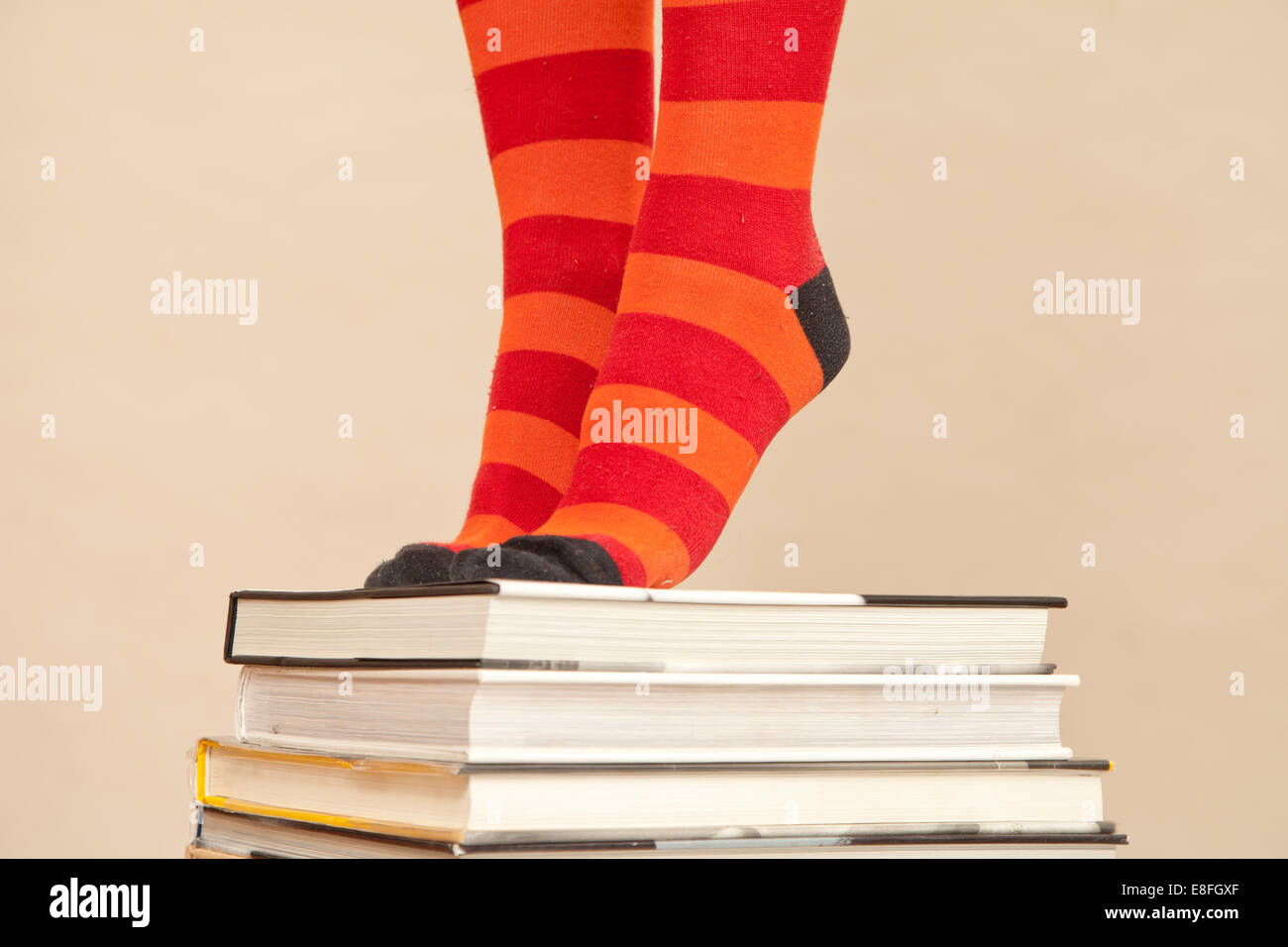 Nahaufnahme einer Frau in gestreiften Socken, die auf Zehenspitzen auf einem Stapel gebundener Bücher steht Stockfoto