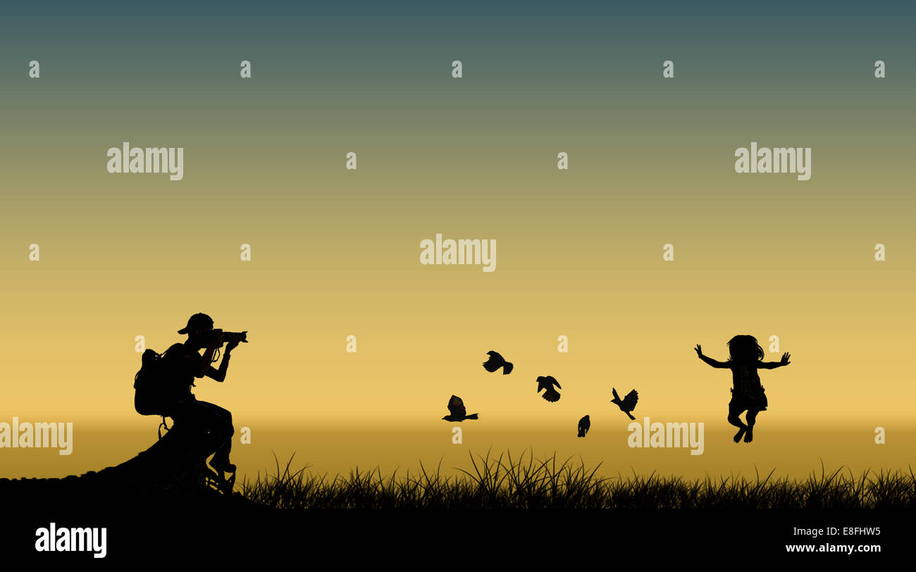 Silhouette eines Fotografen, der ein Foto von einem Mädchen macht, das in der Luft neben fliegenden Vögeln springt, Indonesien Stockfoto