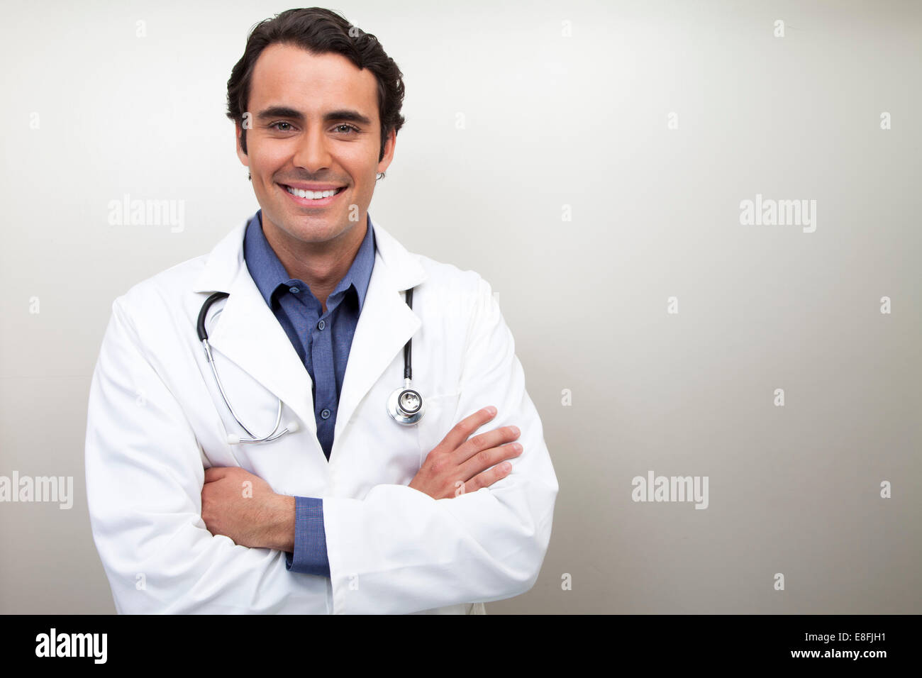 Porträt eines lächelnden männlichen Arztes in einem Labormantel mit gefalteten Armen Stockfoto