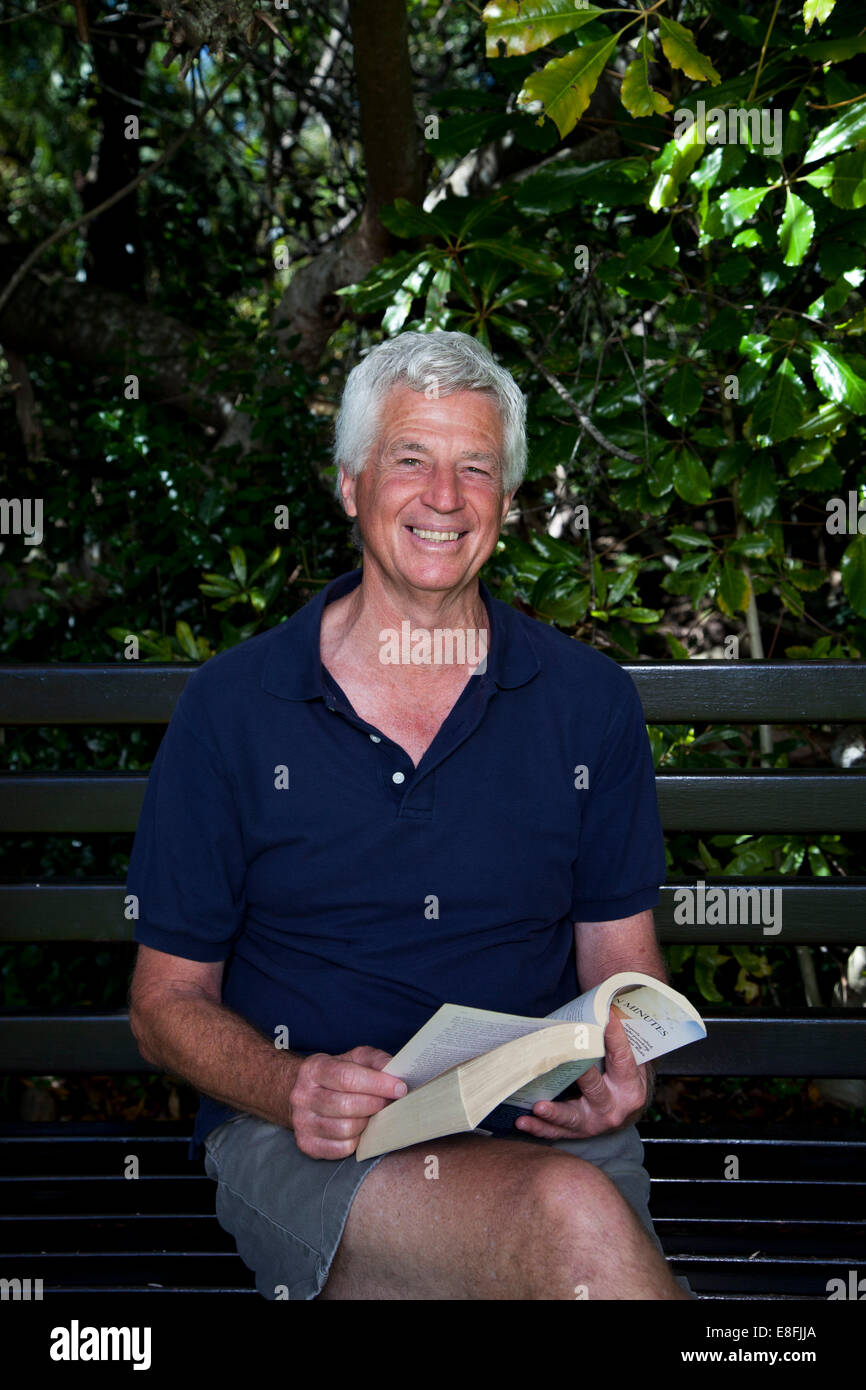 Ältere Mann sitzt auf der Gartenbank mit Buch Stockfoto