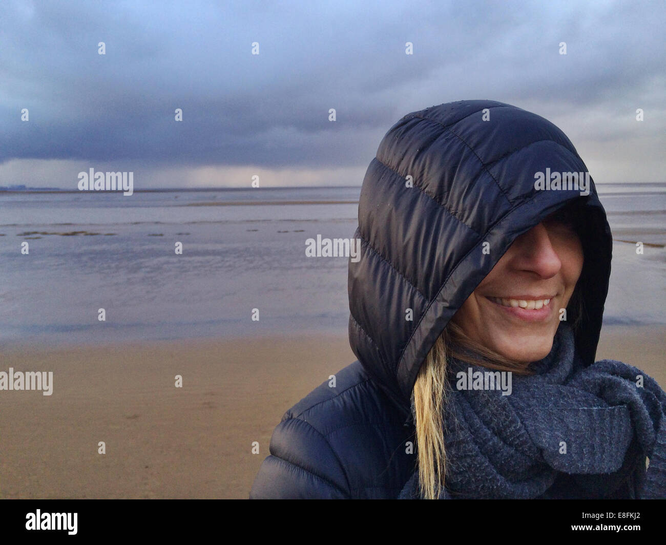 Somerset, UK lächelnde Frau am Strand bei stürmischem Wetter Stockfoto
