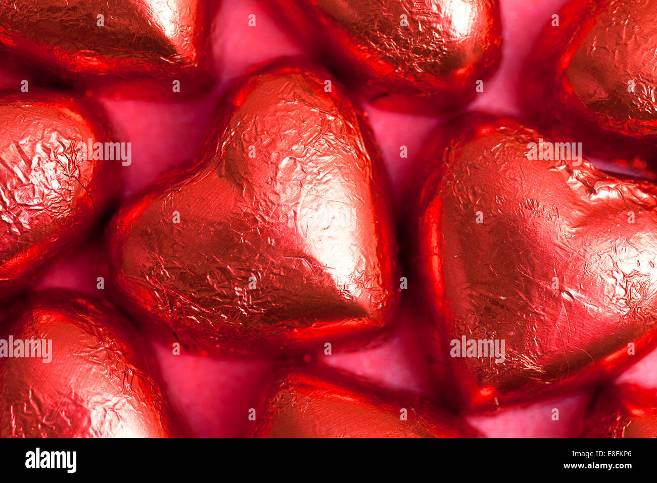 Herzförmige Pralinen in roter Folie auf rotem Hintergrund Stockfoto