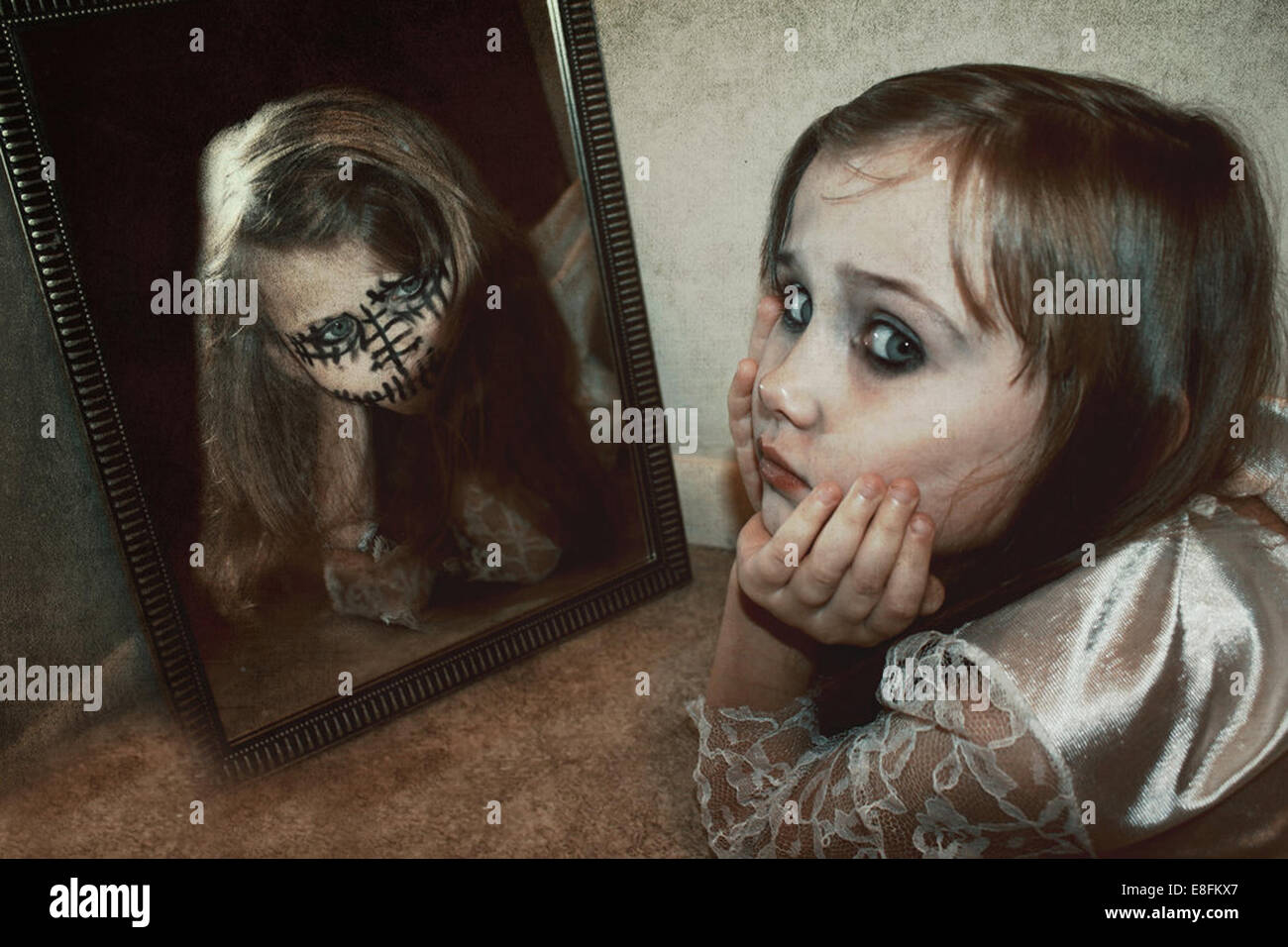 Mädchen auf dem Boden liegend mit einer Reflexion ihres Alter Ego im Spiegel Stockfoto