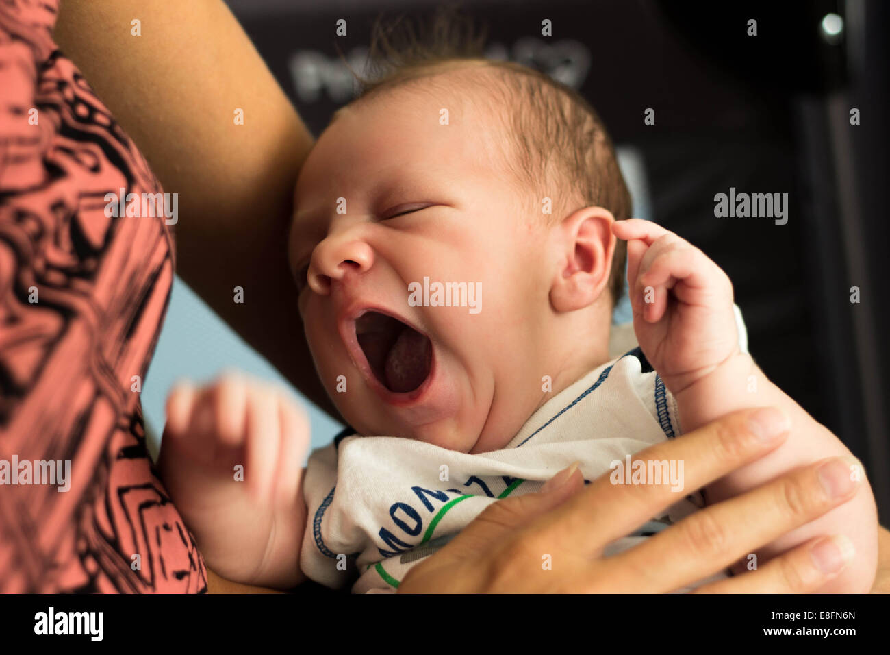 Baby Junge gähnend in den Armen seiner Mutter Stockfoto
