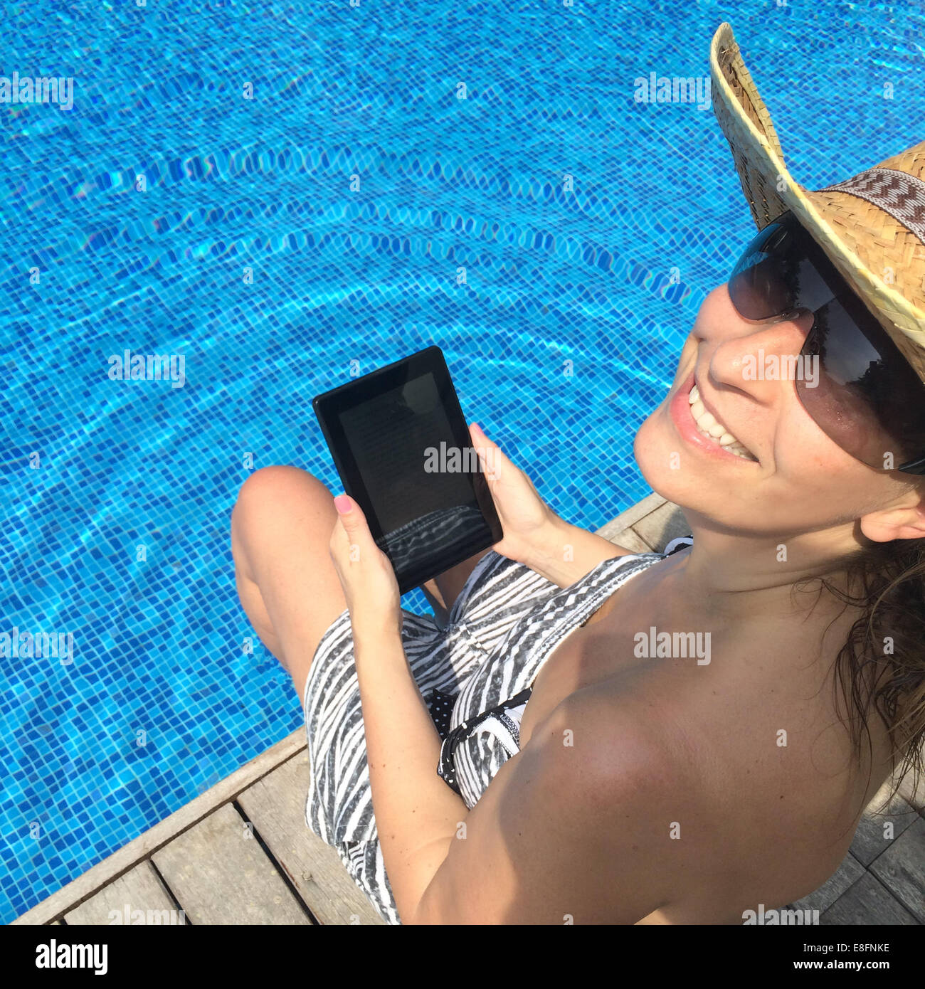 Lächelnde Frau mit digital-Tablette sitzen am Rand des Swimming pool Stockfoto