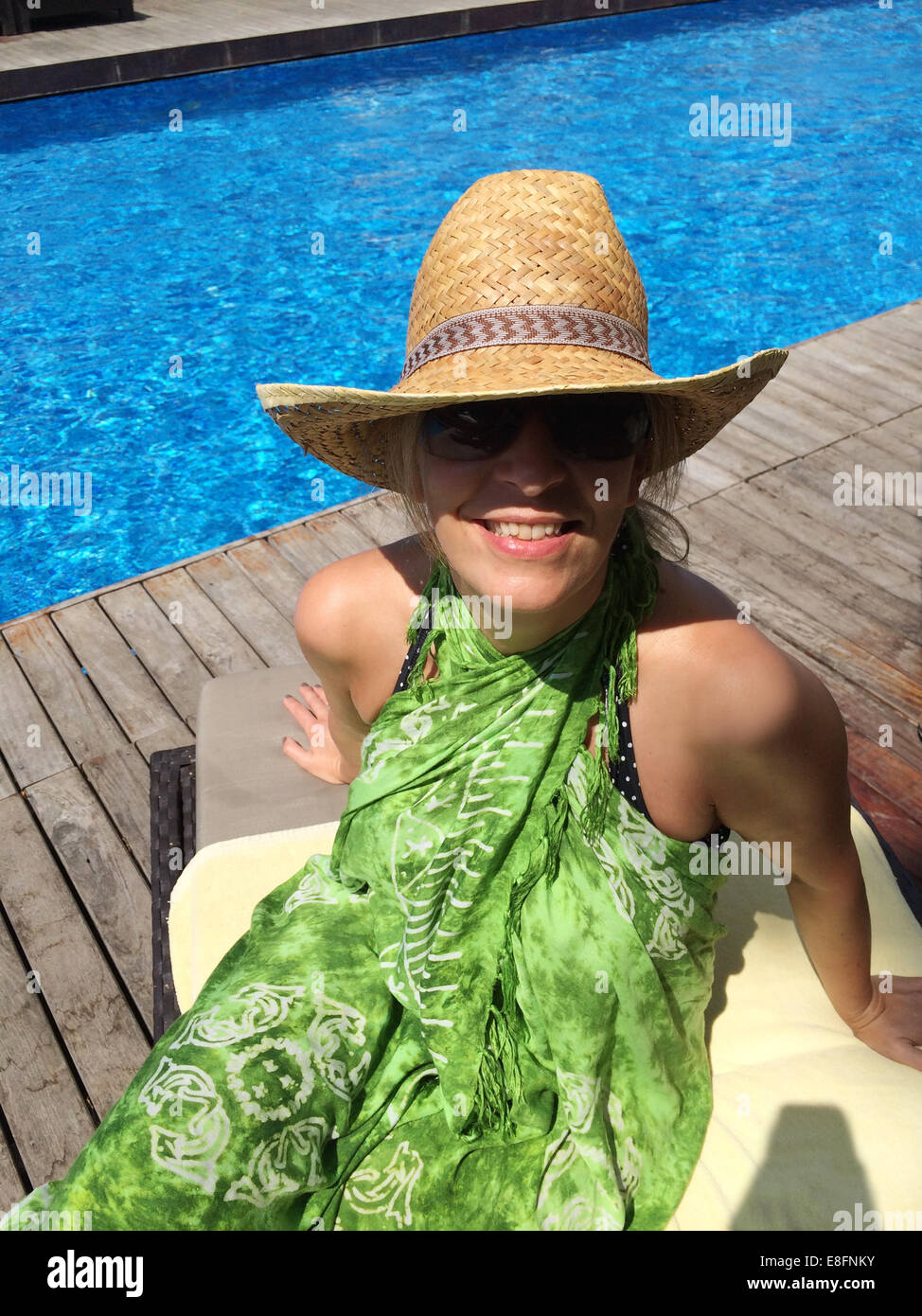 Lächelnde Frau sitzt auf der Liege am Swimmingpool Stockfoto
