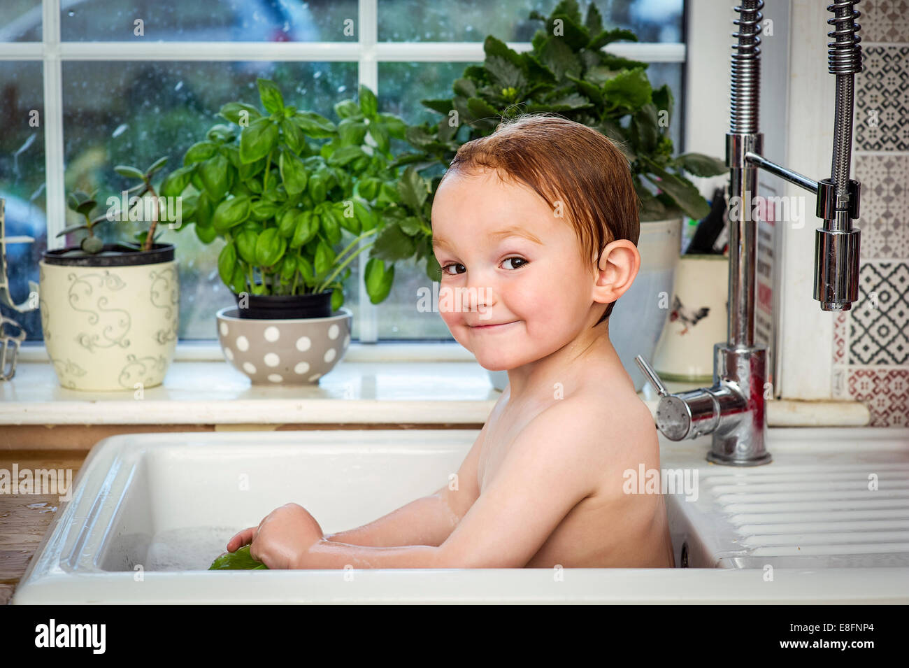Lächelnder Junge, der im Spülbecken der Küche baden kann Stockfoto