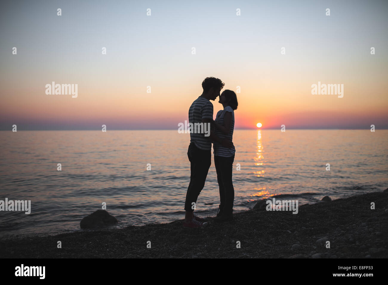 Zwei Teenager stehen am Meer und umarmen sich bei Sonnenuntergang Stockfoto