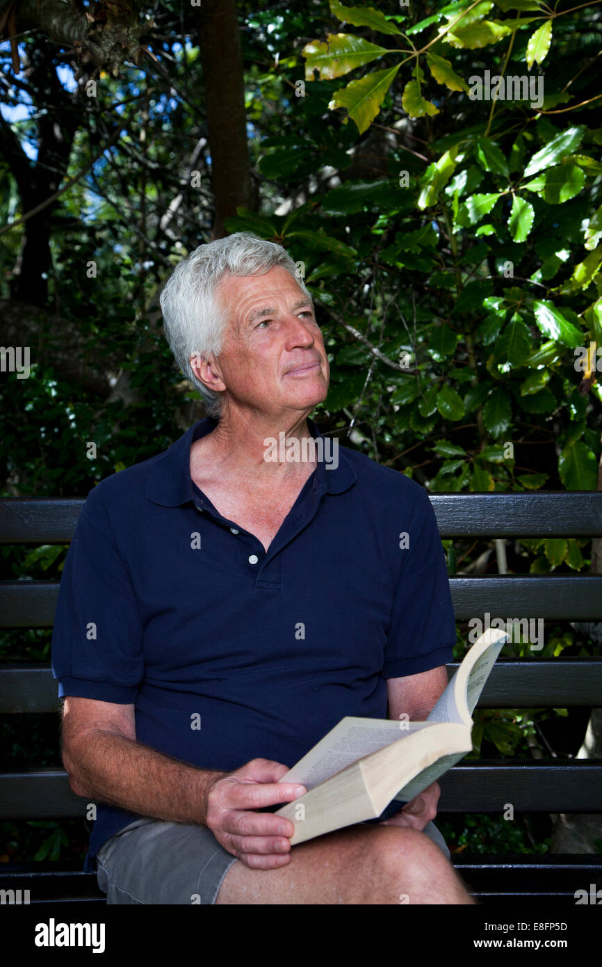 Ältere Mann sitzt auf der Gartenbank mit einem Buch Stockfoto