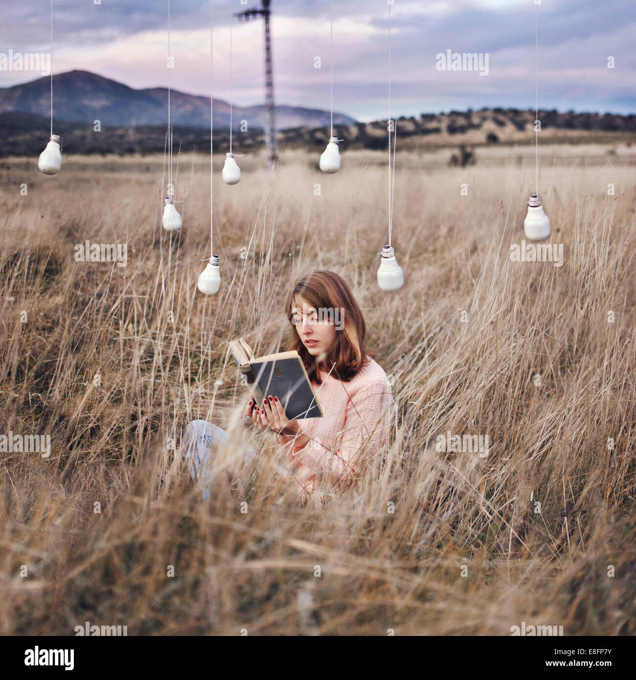 Frau auf einer Wiese unter Energiesparlampen, die ein Buch liest, Spanien Stockfoto