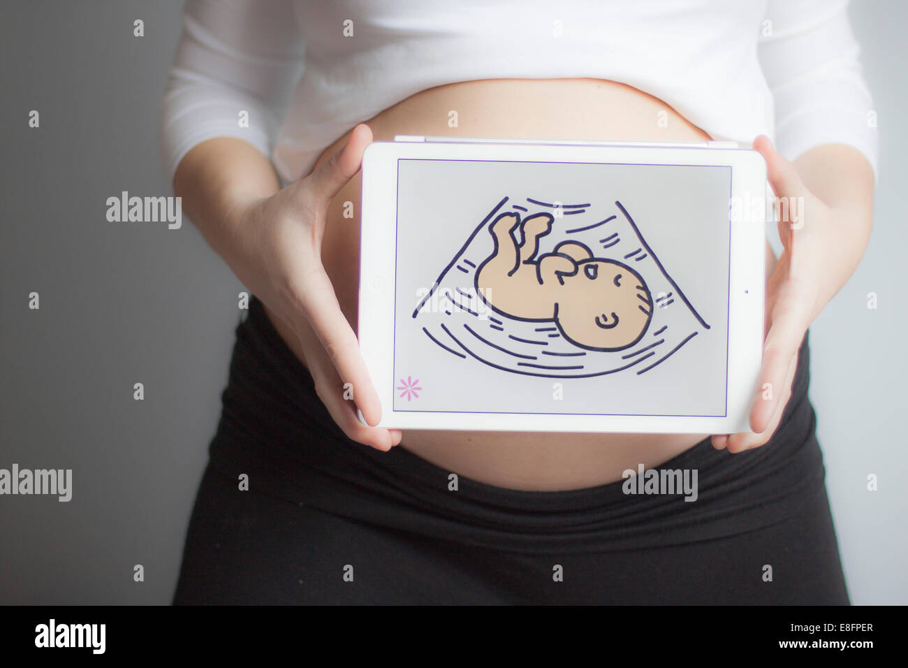 Schwangere Frau, die ein digitales Tablet mit einem Bild eines Babys vor ihrem Bauch hält Stockfoto