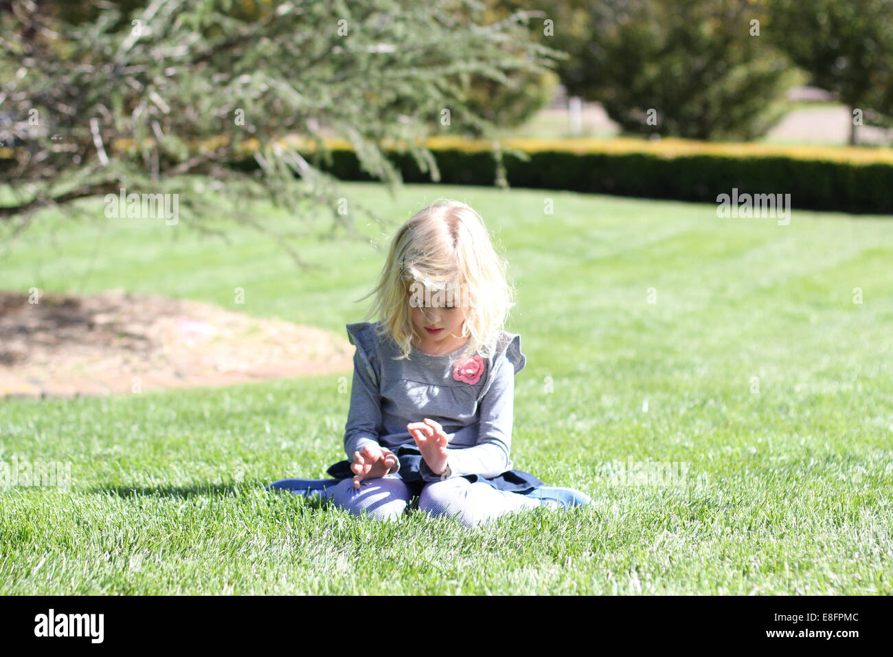 Mädchen sitzen im Garten mit Rasen spielen Stockfoto