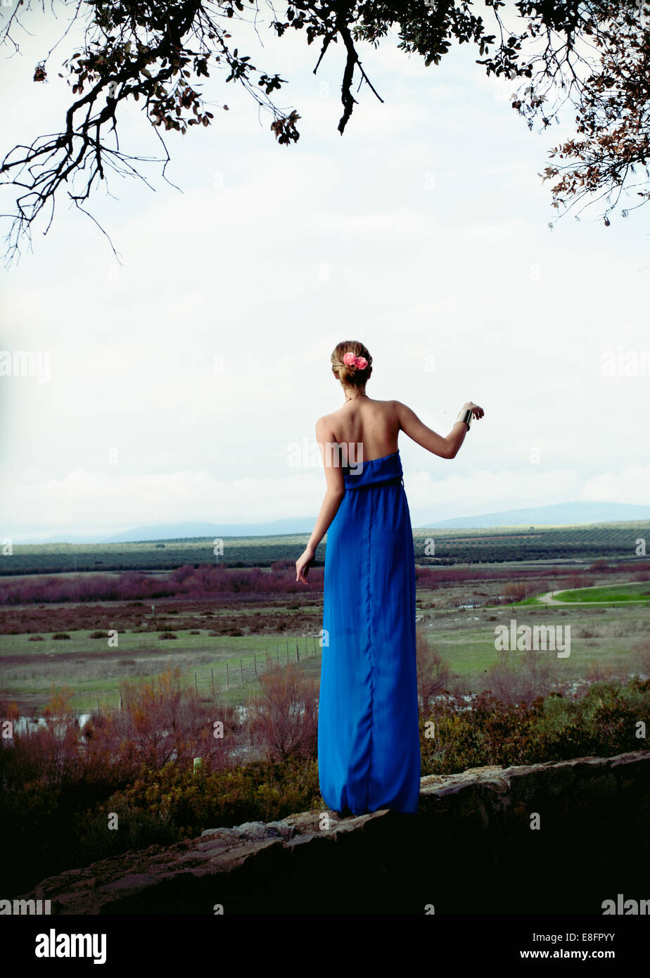 Frau trägt blaue langes Kleid stehend auf Steinmauer Stockfoto