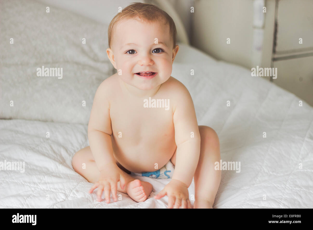 Porträt von Smiling Baby sitzt auf dem Bett im Schlafzimmer Stockfoto
