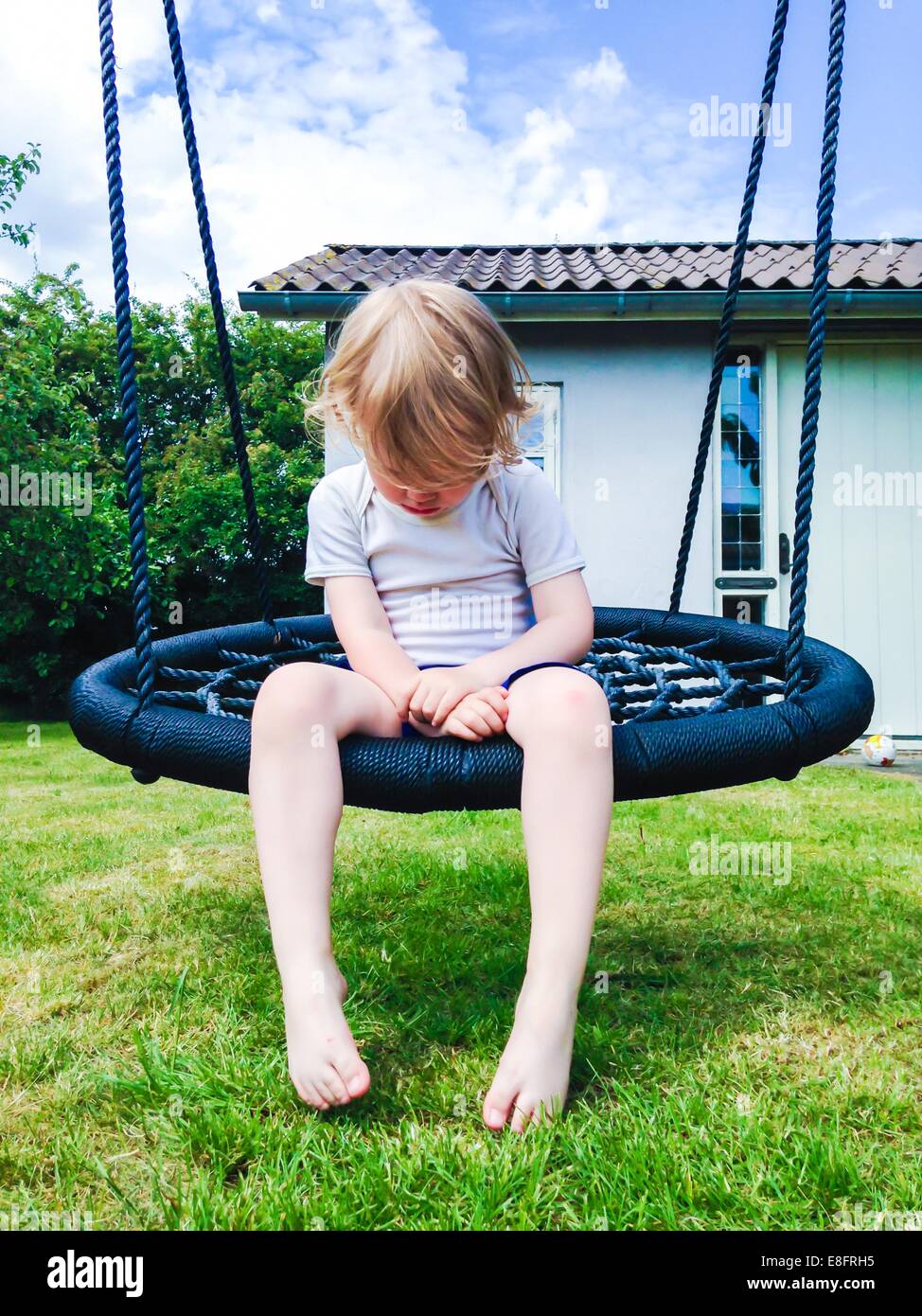 Junge sitzt auf der Schaukel im Garten Stockfoto