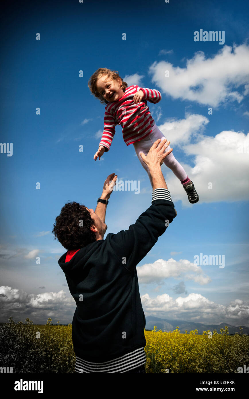 Vater steht auf einem Feld wirft seine Tochter in die Luft Stockfoto