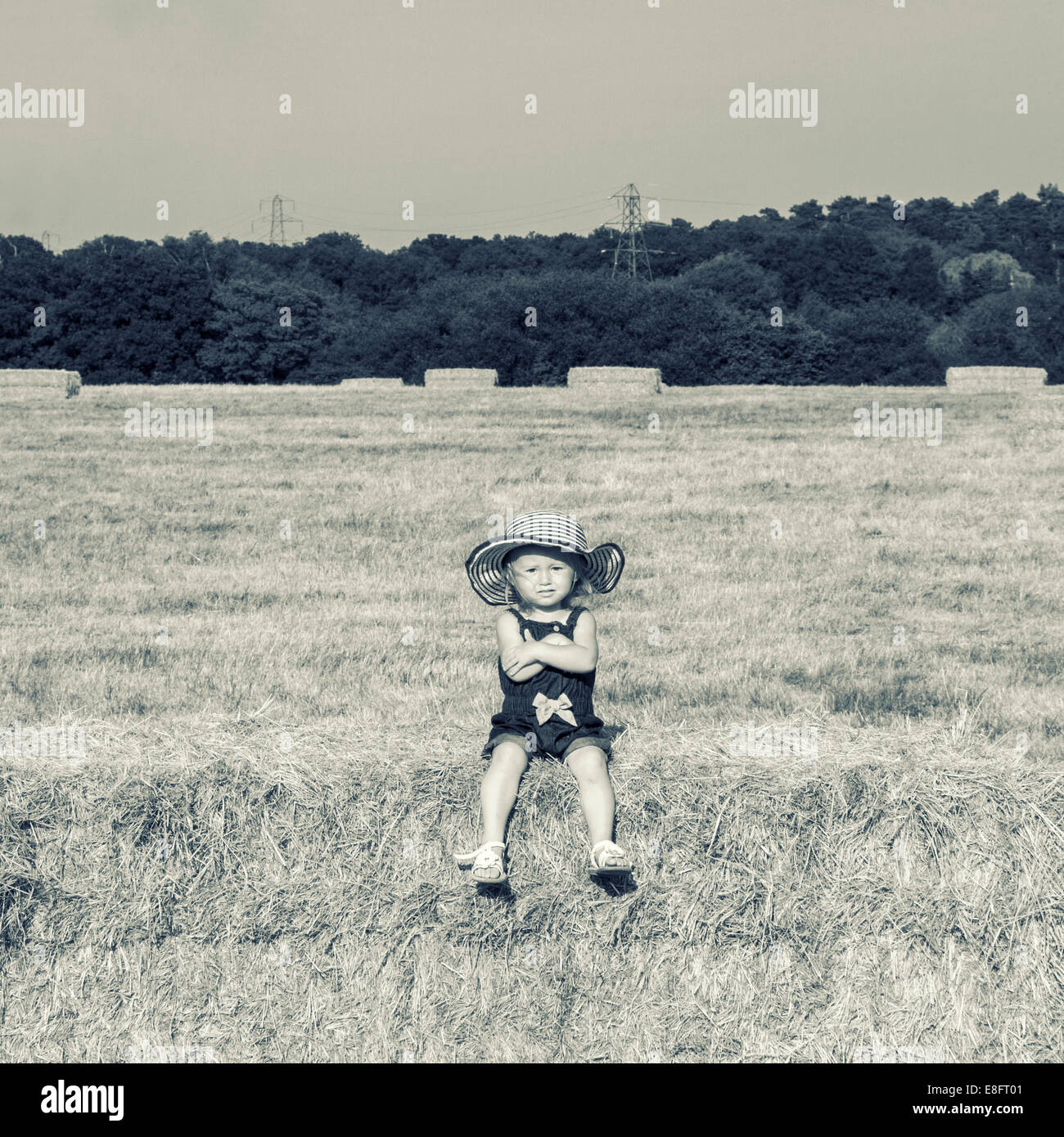 Mädchen sitzen auf Heuballen mit verschränkten Armen Stockfoto