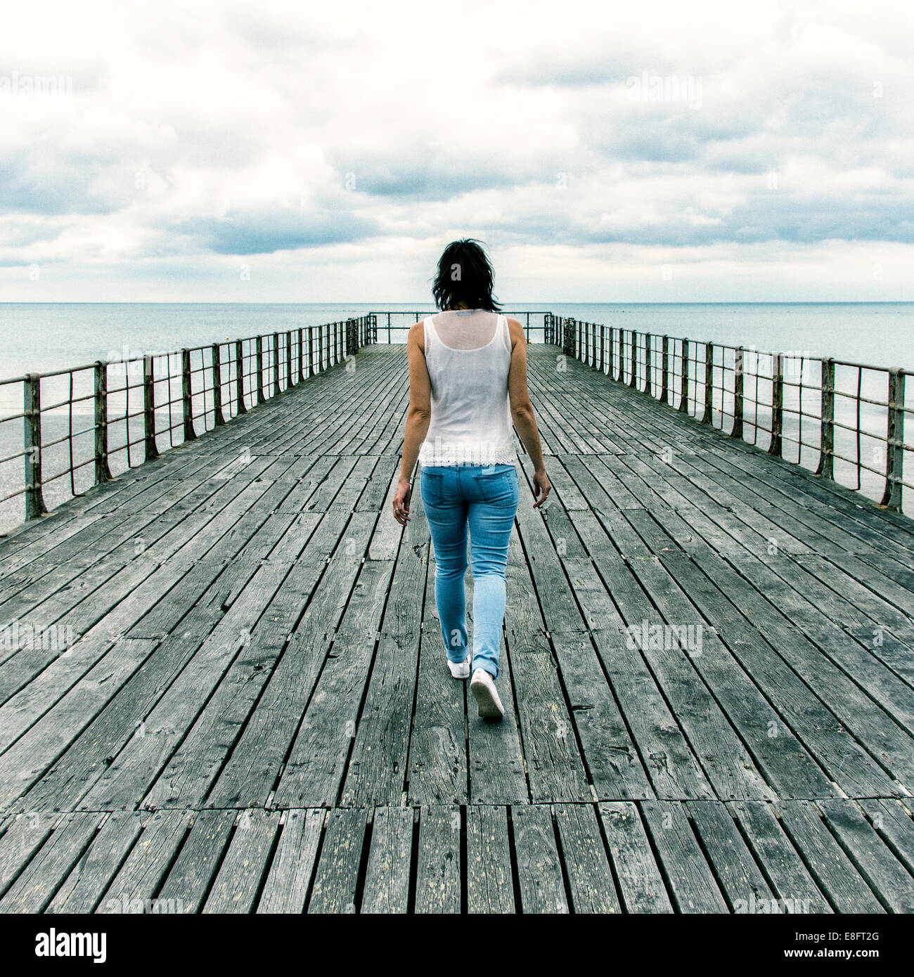 Rückansicht der Frau, die am Pier entlang läuft, England, Großbritannien Stockfoto