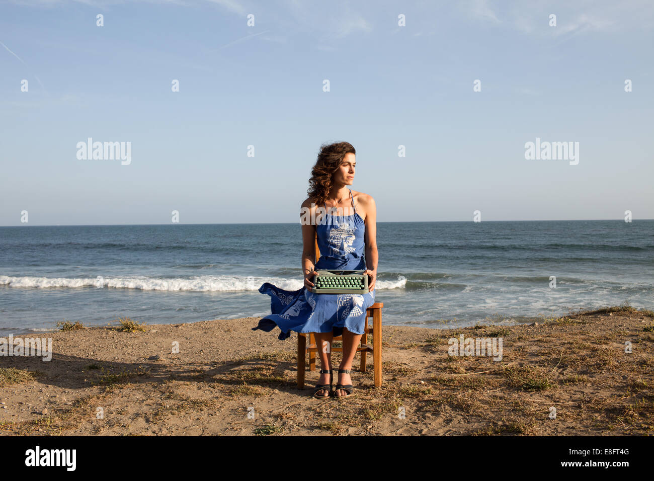 Frau sitzt auf dem Stuhl am Strand mit Schreibmaschine Stockfoto
