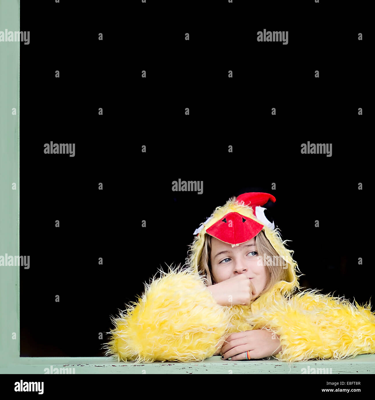 Mädchen, gekleidet in ein Küken Kostüm aus einem Fenster schauen Stockfoto