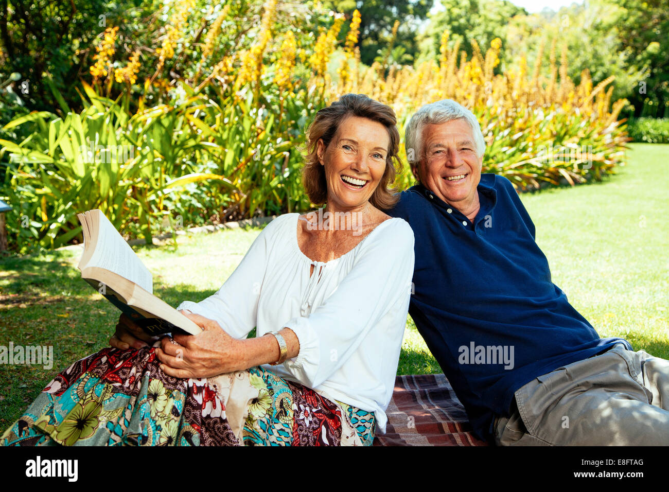Seniorenpaar auf einer Decke sitzen und sich im Garten entspannen Stockfoto