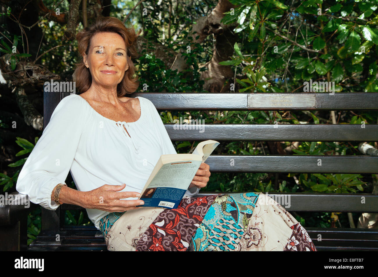 Ältere Frau entspannend im Garten mit einem Buch Stockfoto