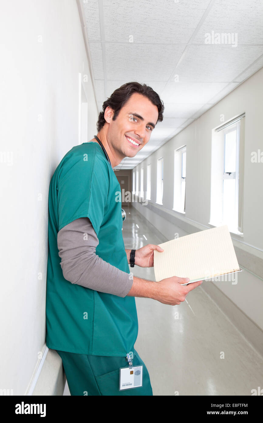 Porträt eines lächelnden männlichen Arztes, der im Krankenhausflur steht und medizinische Notizen ansieht Stockfoto