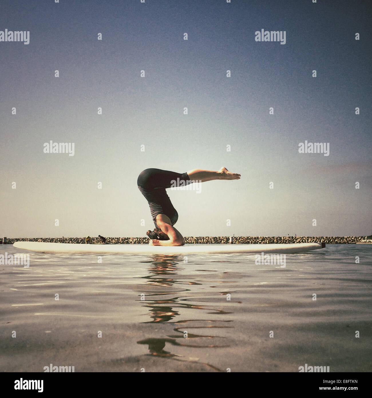 Frau, die einen unterstützten Yoga-Kopfstand auf einem Paddleboard macht, kalifornien, amerika, USA Stockfoto