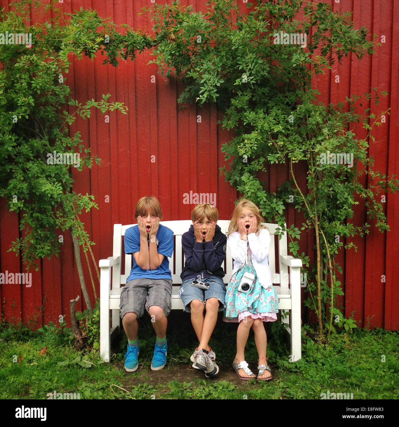 Drei Kinder sitzen auf Bank im Garten Stockfoto