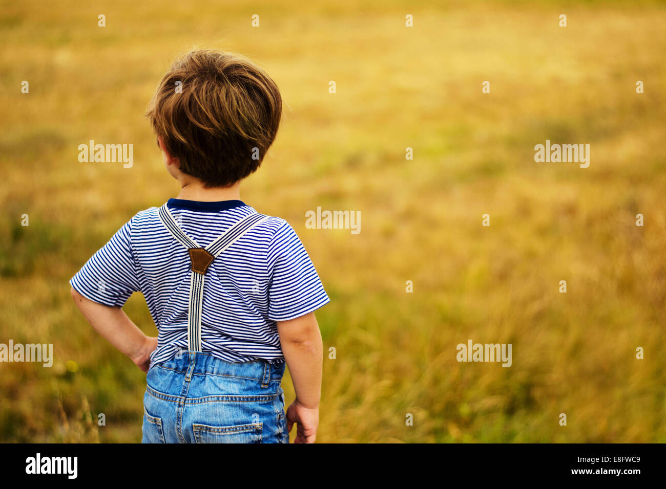 Junge, der mit der Hand auf der Hüfte auf einem Feld steht Stockfoto