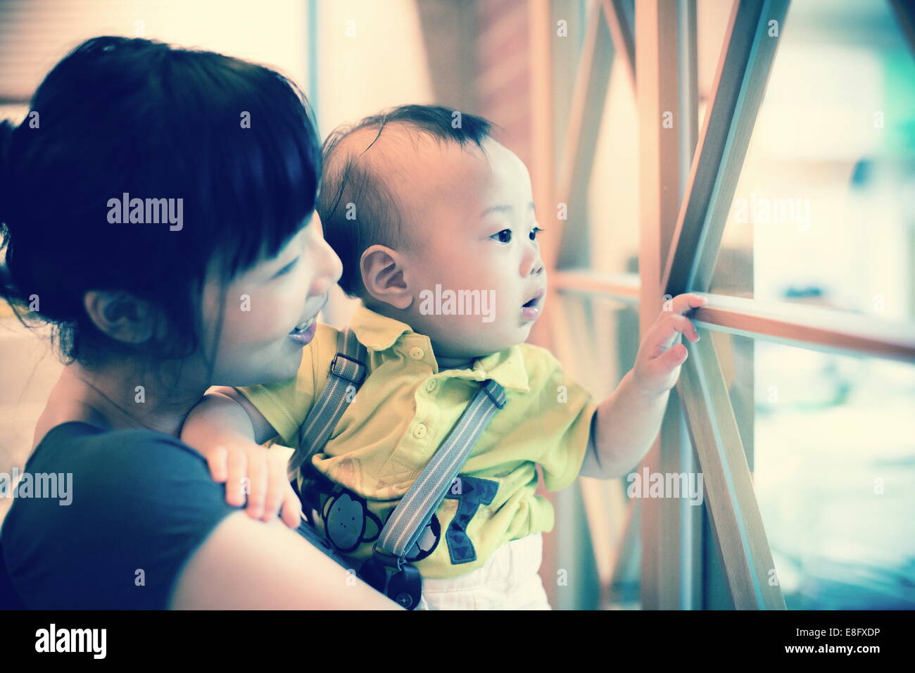Mutter und ihr kleiner Sohn schauen durch ein Fenster Stockfoto