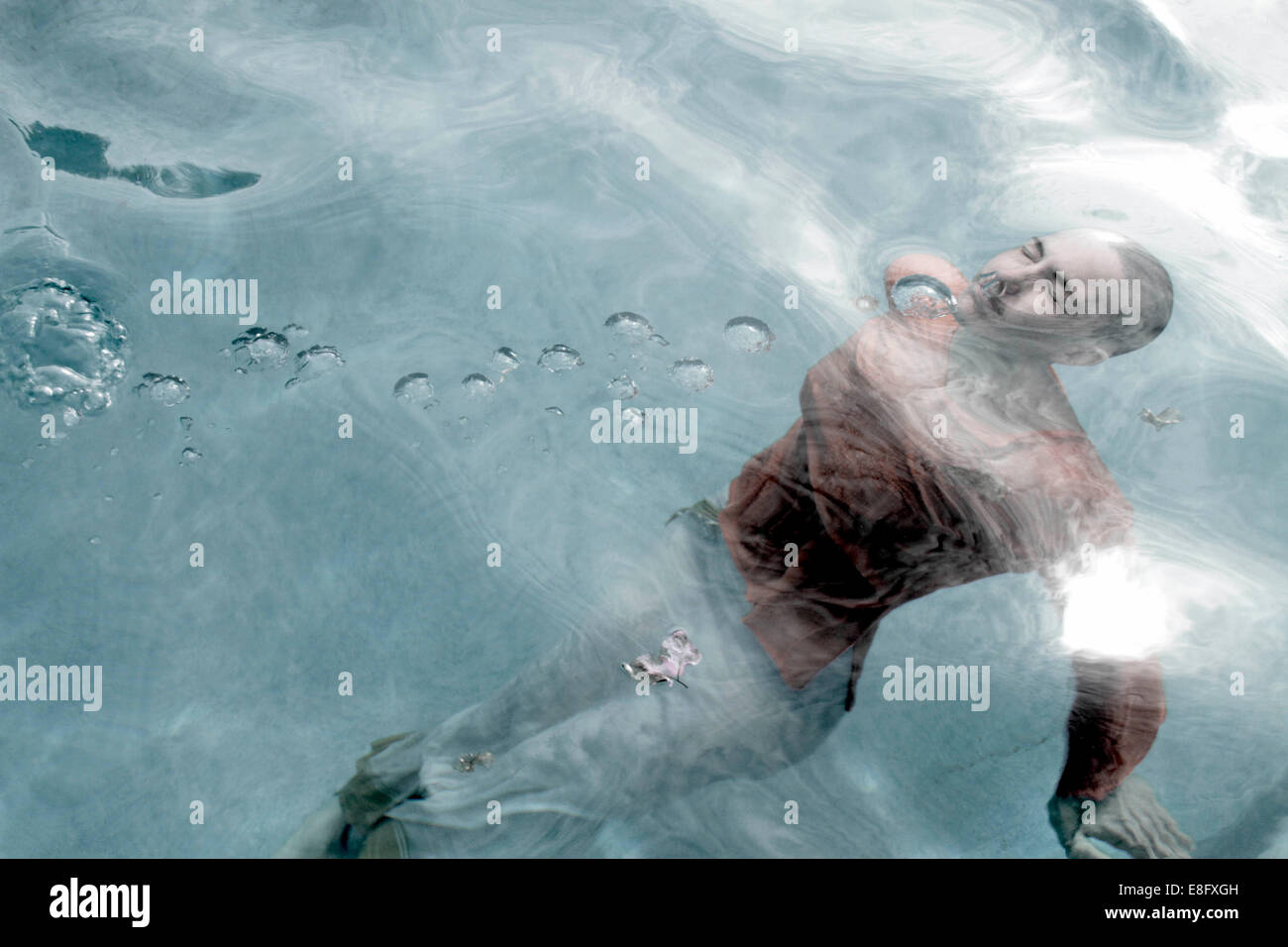 Voll bekleidete Frau mit geschlossenen Augen schwimmend unter Wasser in einem Schwimmbad Stockfoto