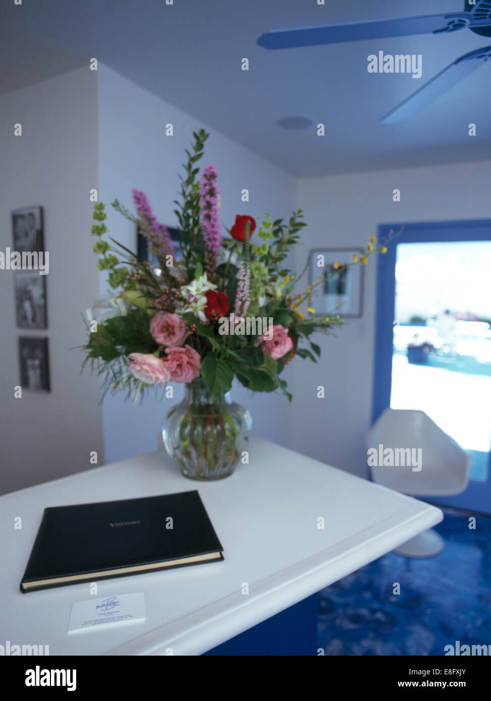 Vase mit Sommerblumen und Gästebuch auf Schreibtisch im modernen Hotel-Rezeption Stockfoto