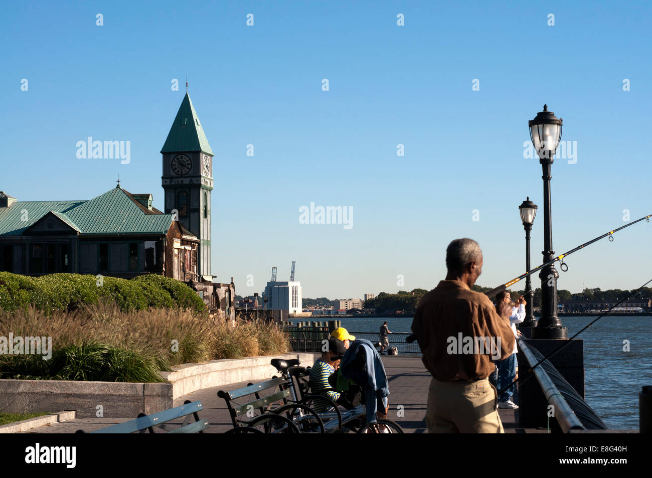 Menschen zu Fuß, ist laufen, Fahrrad und Angeln im Pier A. Pier A im Battery Park ein Gebäude, erbaut 1886 von der Abteilung für Stockfoto