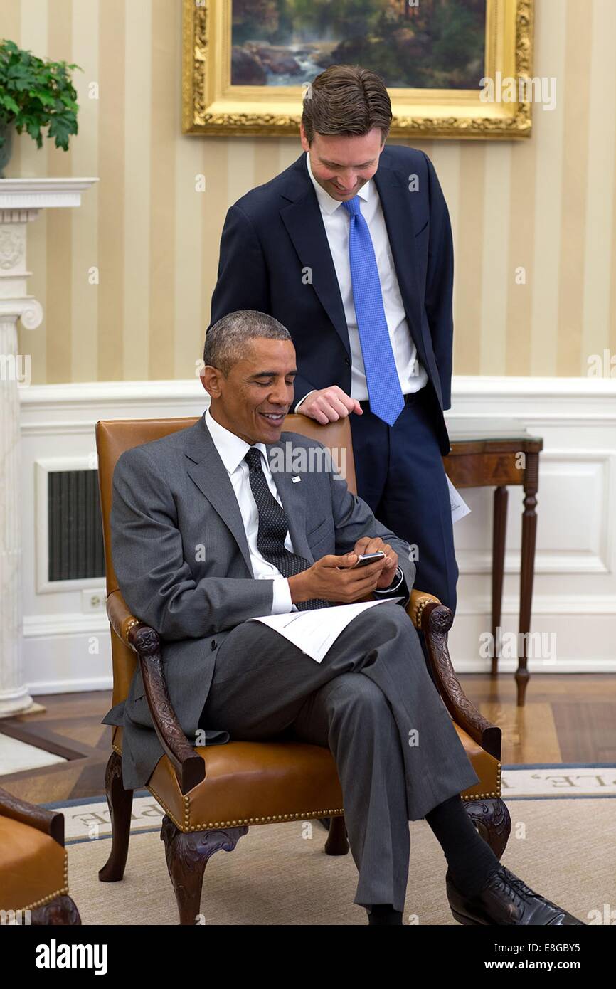 US-Präsident Barack Obama sieht auf Fotos von Pressesprecher Josh Earnest neugeborenes Baby Boy, Walker, während eines Treffens mit senior Berater im Oval Office des weißen Hauses 25. August 2014 in Washington, DC. Stockfoto