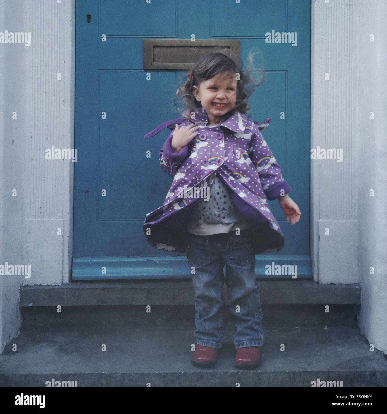 Lächelndes windswept Mädchen, das vor einer Haustür steht, London, England, Großbritannien Stockfoto