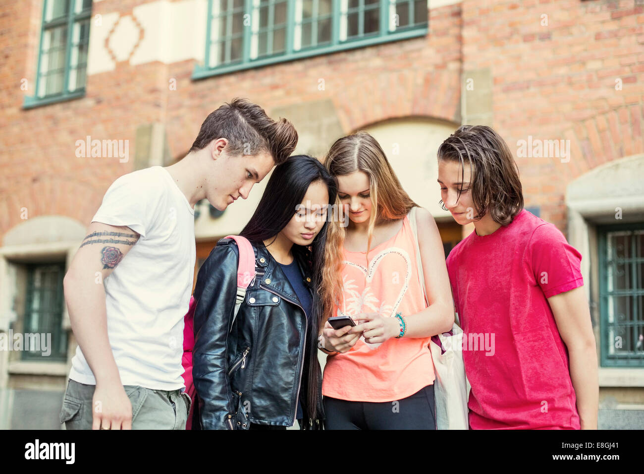 High-School-Freunde lesen SMS auf Handy im Schulhof Stockfoto