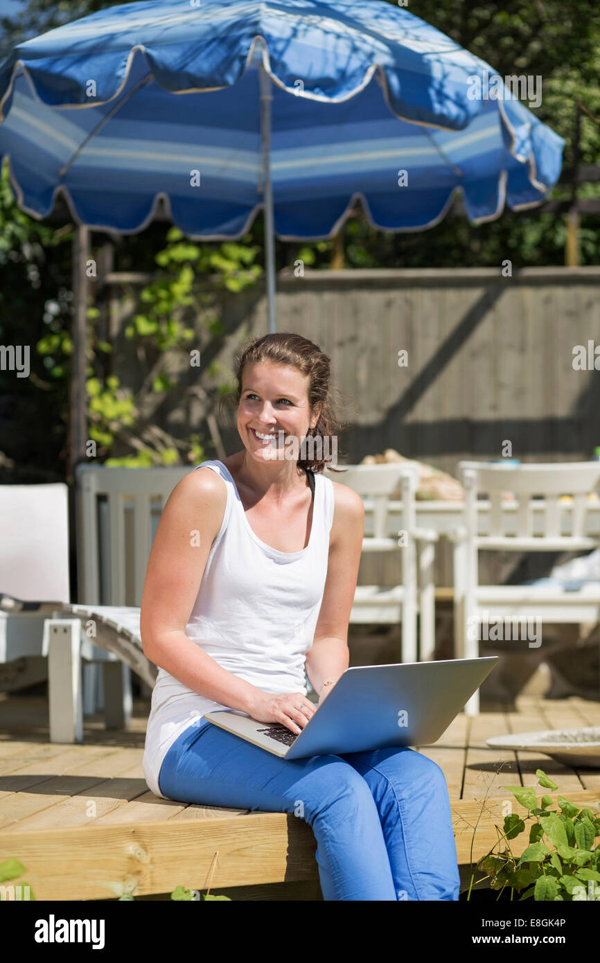 Glücklich Mitte Erwachsene Frau mit Laptop entspannend auf Terrasse Stockfoto