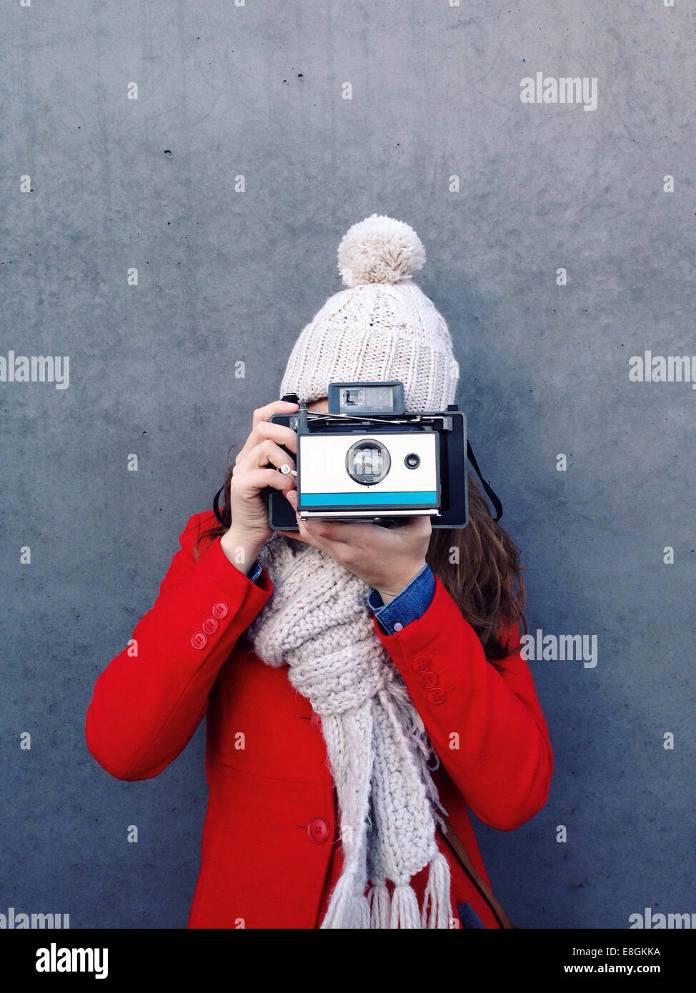 Junge Frau, die vor einer Wand steht und mit einer Sofortkamera fotografiert Stockfoto