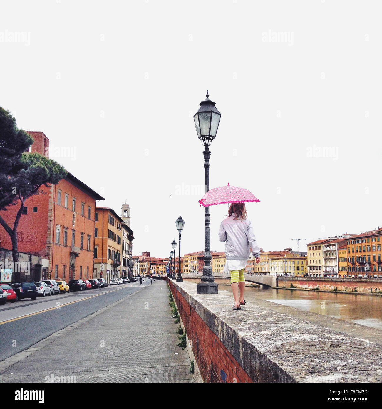 Mädchen, die im Regen an einer Mauer entlang laufen, Pisa, Toskana, Italien Stockfoto