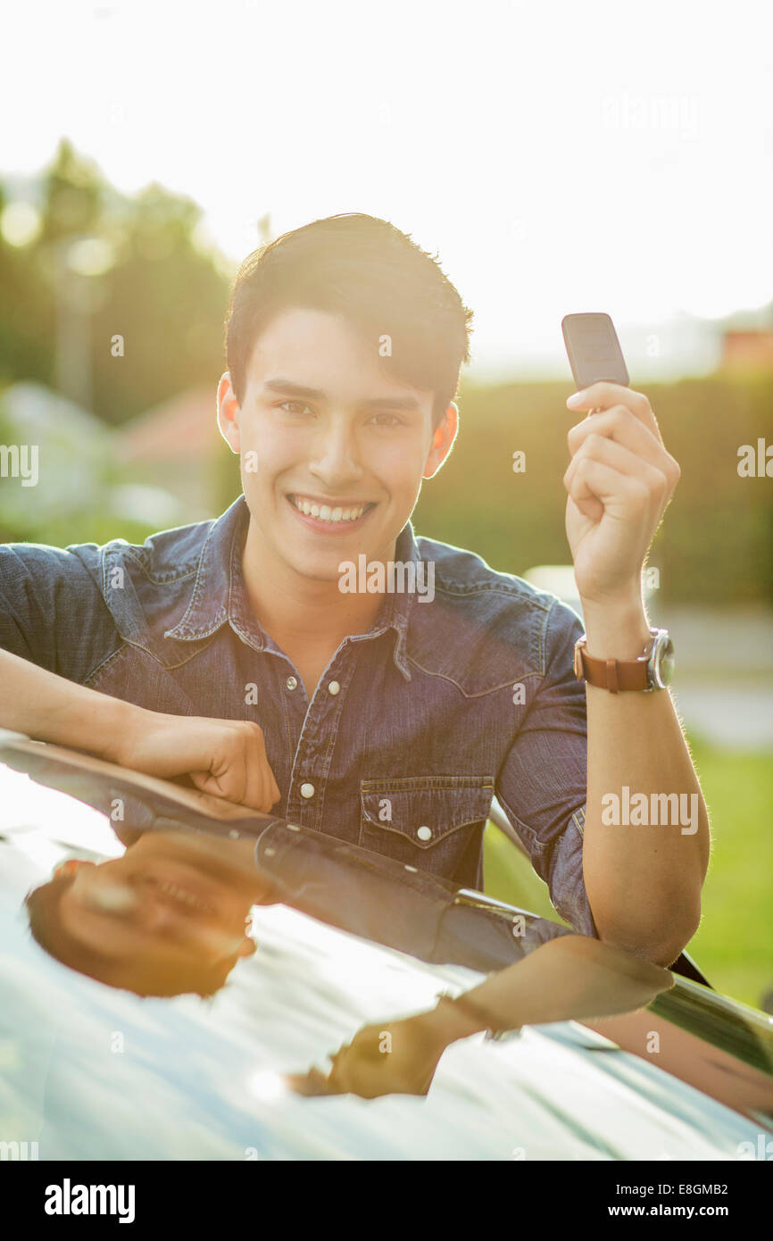 Porträt von glücklicher junge Mann zeigt Schlüssel beim stützte sich auf Auto Stockfoto