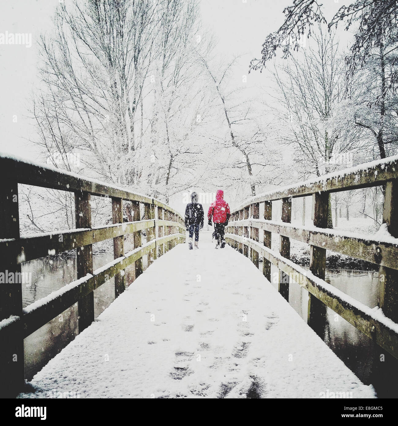 Rückansicht von zwei Kindern, die im Schnee über den Steg laufen Stockfoto