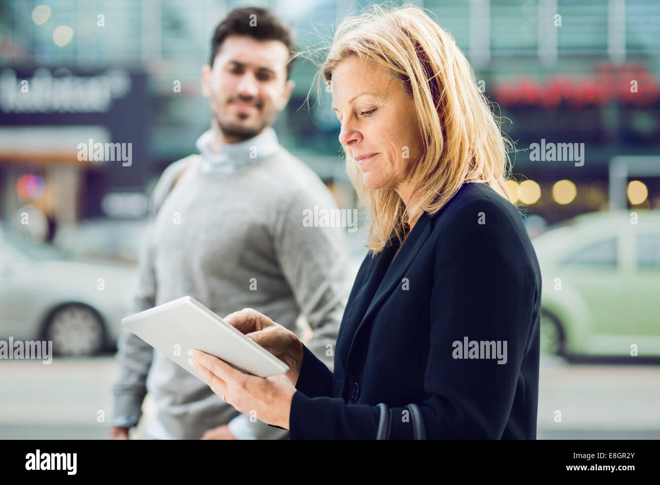 Seitenansicht der Geschäftsfrau mit digital-Tablette auf Stadtstraße mit Kollegen im Hintergrund Stockfoto